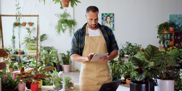 Man in apron using tablet in a plant shop.