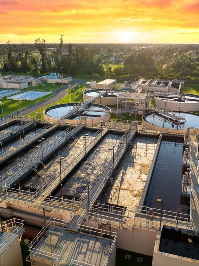 Water treatment plant at sunset with circular tanks and greenery.