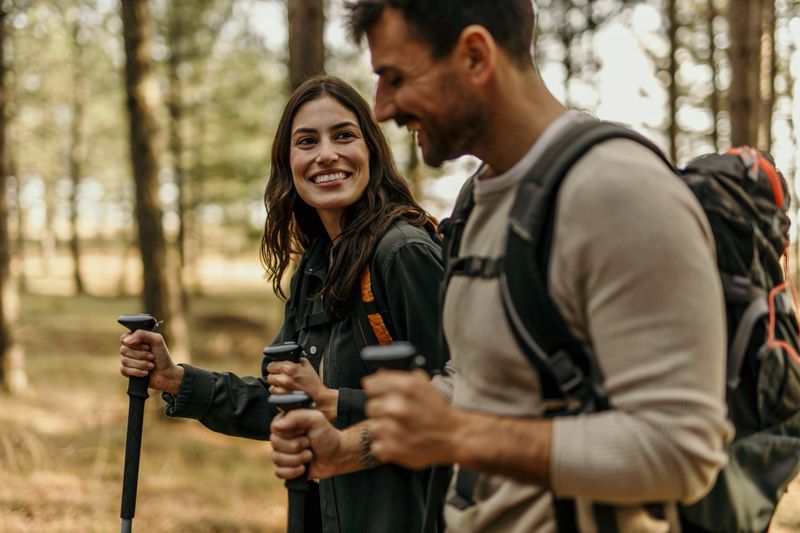 Young smiling couple enjoying a hike through the forest using trekking poles and backpacks
