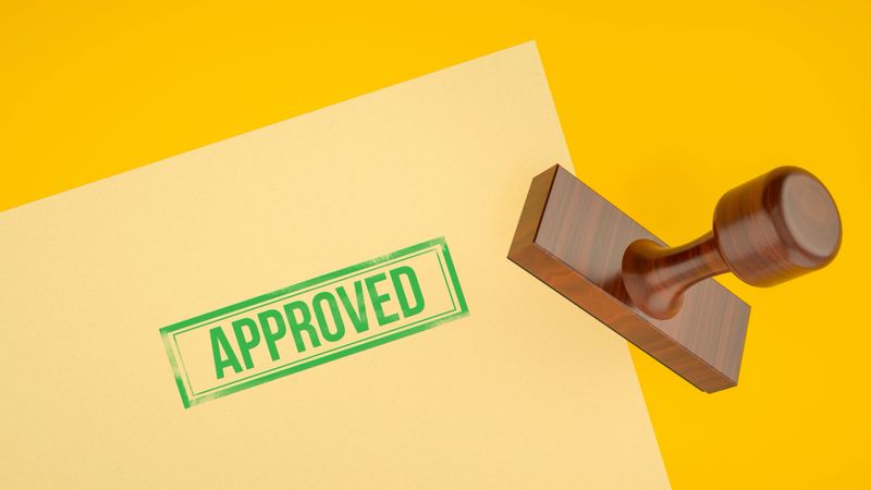 This 3D illustration shows a wooden Stamp pressing the word "APPROVED" in green ink onto a document. The Top View and clean composition create a clear and direct message of Validation, Acceptance, and Success. This is a versatile visual for a wide range of Business and Finance topics, including loan Application Form approvals, passing a Quality Control check, or finalizing a Contract. The Green color reinforces the Positive Emotion associated with the approval.