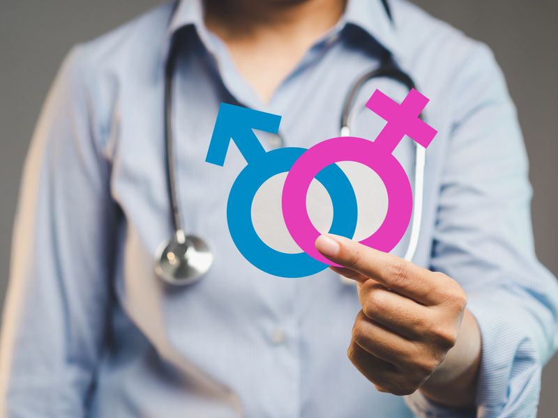Close-up of doctor in blue shirt holding male and female symbols, representing gender health, medical identity, equality, and inclusive care in healthcare and wellness contexts.