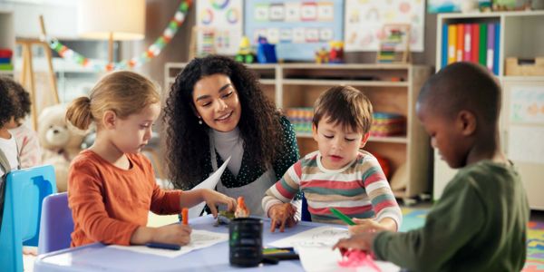 Teacher helping young children with coloring activities in classroom.