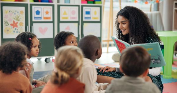 A teacher reads a book to a group of attentive young children in a colorful classroom.