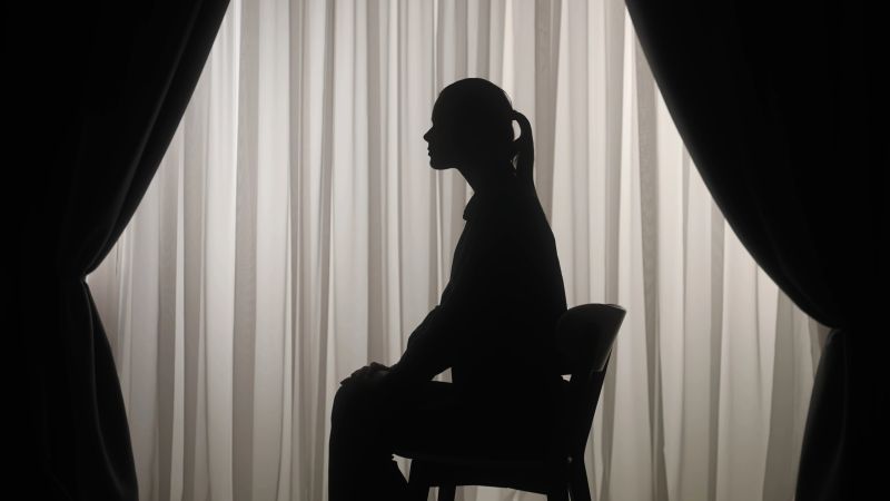 Silhouette of a woman sitting in front of softly lit curtains expresses upset, stress and introspection. Mental Health Concept.