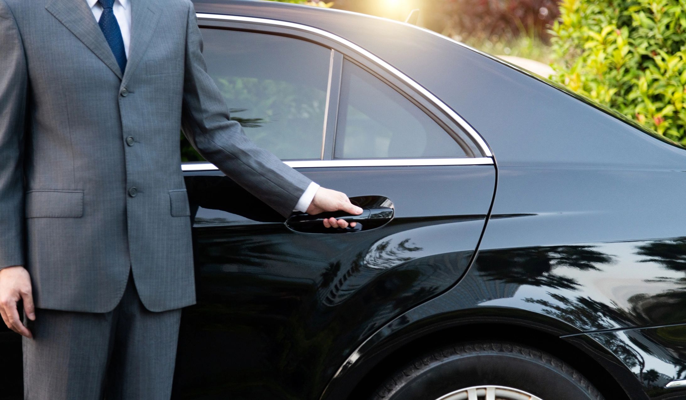 Man in a suit opening a black luxury car door.