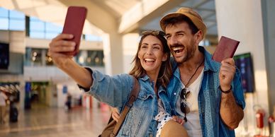A happy couple takes a selfie at the airport holding passports.