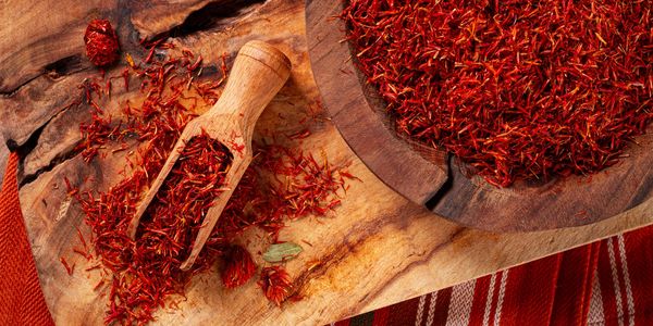 Dried saffron threads on a wooden surface with a scoop.