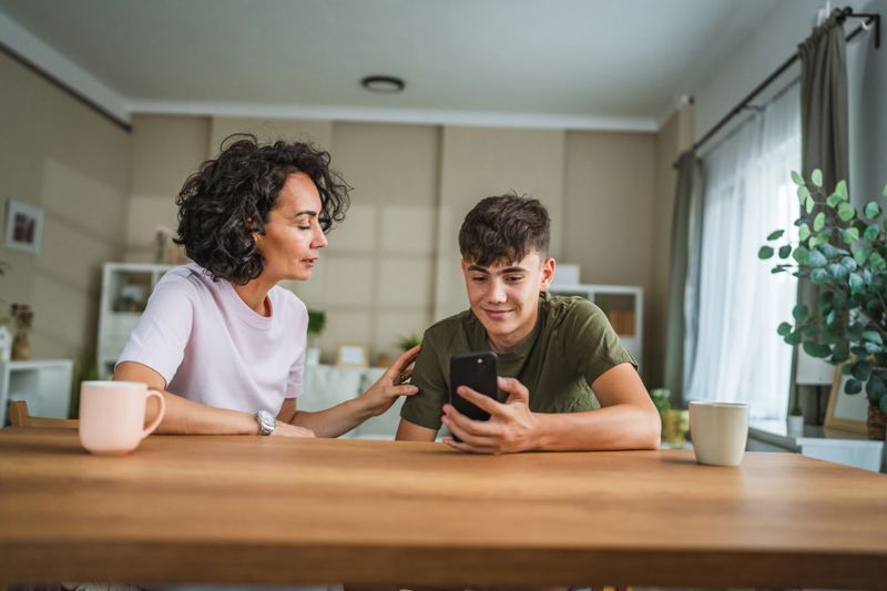 talk mother support and solving problem together with teenage boy son, share experience and opinion boy hold mobile phone