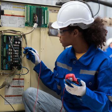 Female electrician testing an electrical panel with tools.