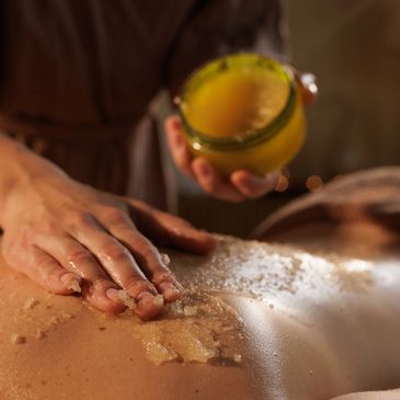 Hand applying scrub to back with jar of scrub paste.