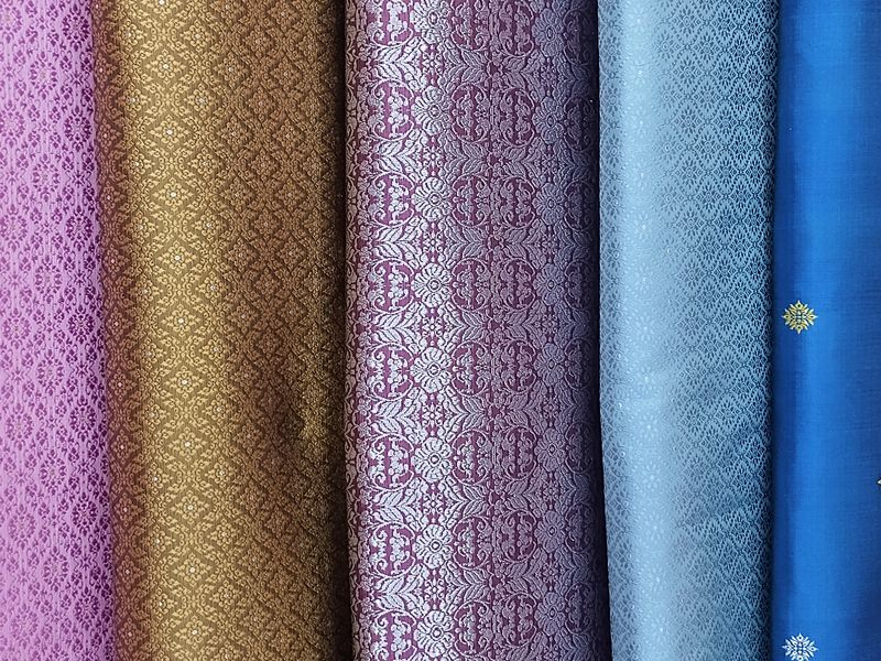 A stunning collection of exquisite silk cloth, meticulously crafted with detailed patterns, reflecting light beautifully across their diverse and rich hues.