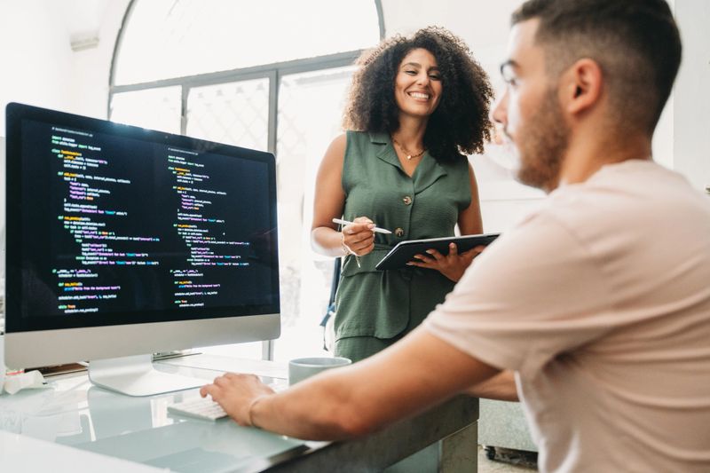 Two software developers collaborating on a project, discussing code while analyzing the computer screen in a bright, modern office