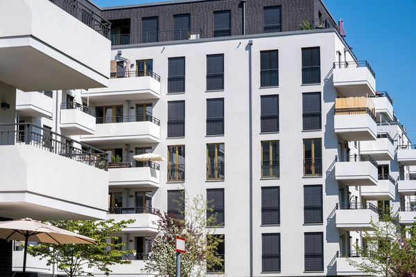 A beige and white apartment building with balconies and chimneys is surrounded by trees.