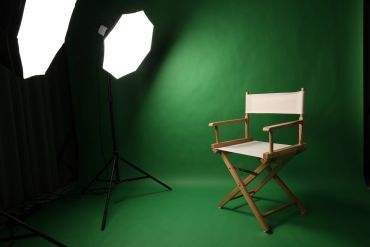 A director's chair in a green studio with bright lights.