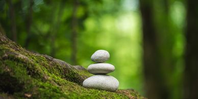 Stack of balanced stones on mossy ground in a serene forest.