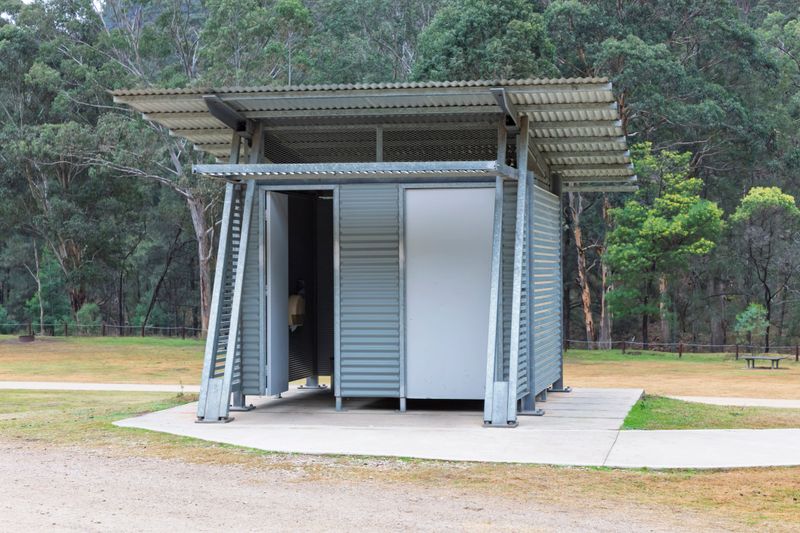 Photograph of a reasonably well maintained steel and corrugated iron unisex toilet block on a concrete base located in a large public use campground facility.
