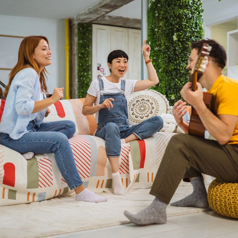group of multicultural people have fun together at modern flat. Happy caucasian man playing the guitar enjoying time with his female friends at home