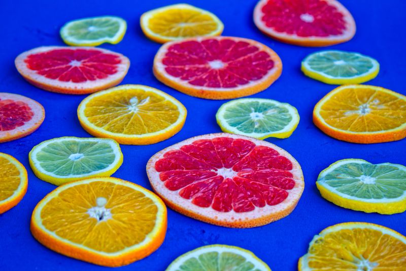 Colorful Citrus And Kiwi Fruit Slices Arranged On A Bright Blue Background, Displaying A Fresh And Vibrant Composition With Grapefruit, Lemon, Orange, Lime, Blueberries, And Green Leaves