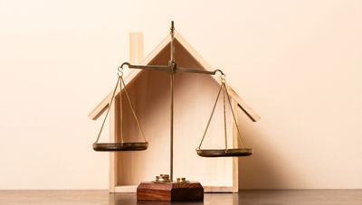 A balance scale in front of a wooden house model.