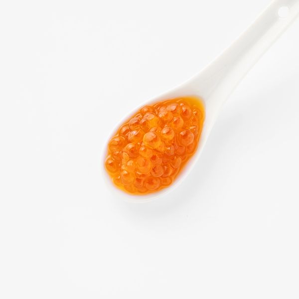 White spoon with orange salmon roe against white background.