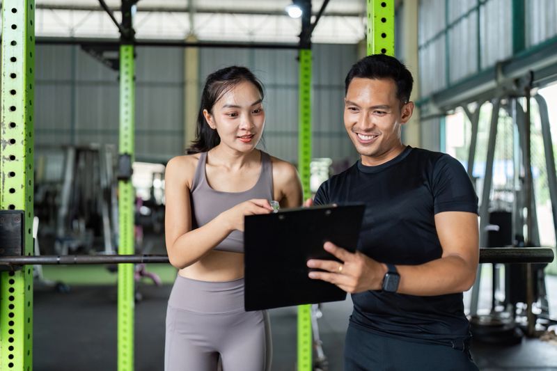 A personal trainer assists a client in a gym, providing workout tips and motivation during a training session.