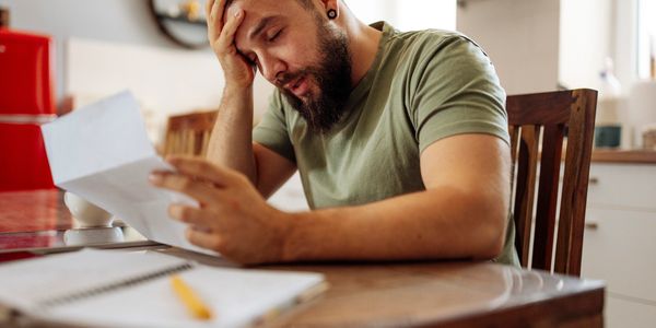 Stressed man reading a document at home, holding his head in frustration.