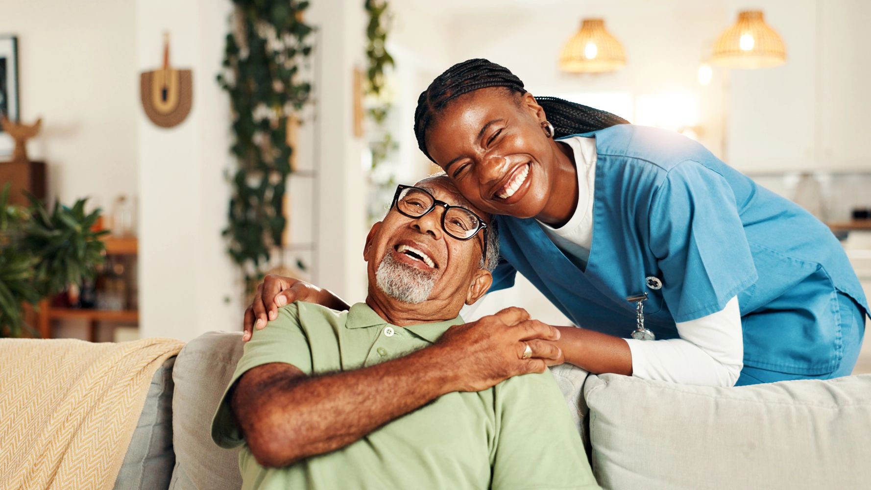 Caregiver and elderly man smiling together indoors.
