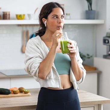 Woman in workout clothes drinking green smoothie in kitchen.