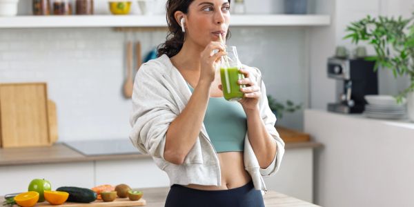 Woman drinking green smoothie in kitchen.