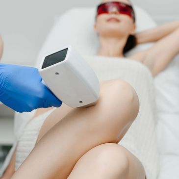 Woman receiving laser hair removal treatment on her leg in a clinic.