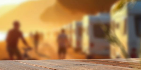 Wooden table with blurred background of people and RVs at sunset.