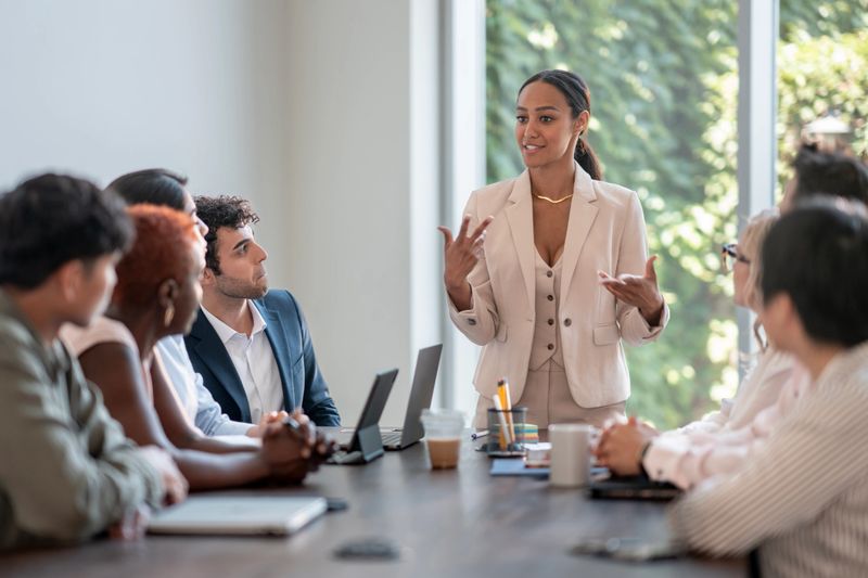 Corporate professionals collaborate and engage in a productive business meeting, with a leader presenting effectively, promoting teamwork, communication, and strategy development in a focus-driven modern workspace surrounded by natural light.
