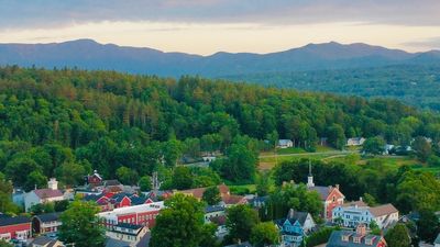 A town nestled by forested hills and distant mountains at sunset.