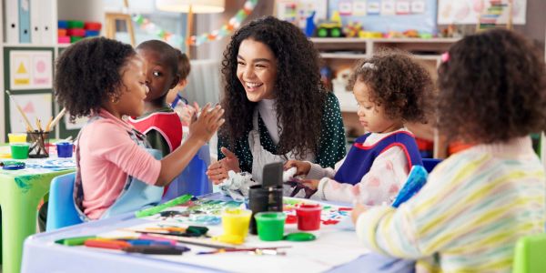 Happy teacher engaging with young children in a colorful classroom art activity.