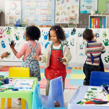 Children making handprint art in a colorful classroom.