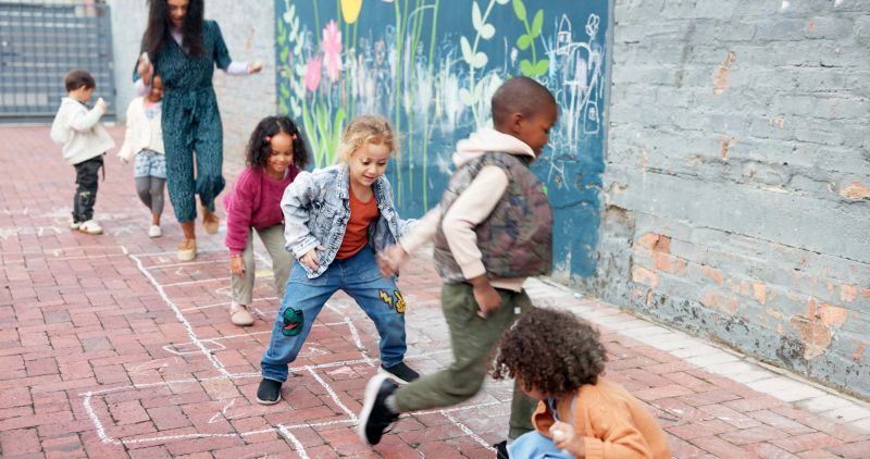 Kindergarten, children and outdoor playing with teacher for childhood development, game or hopscotch. Group, kids or learners jumping with fun activity at school for hopping or skipping on playground