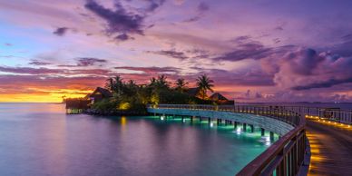 Sunset over tropical island with illuminated walkway.