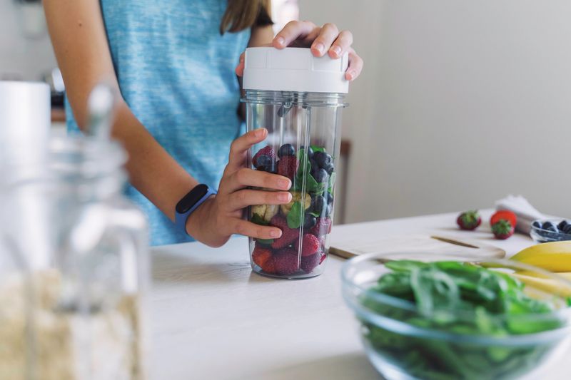 A girl focuses on blending fresh fruits and greens for a nutritious smoothie, perfectly illustrating the balance of health and enjoyment in everyday cooking.