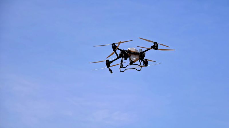 Industrial drone flying in clear blue sky. An agricultural drone equipped with multiple rotors is flying in the sky, used for crop monitoring, spraying, or farm management.