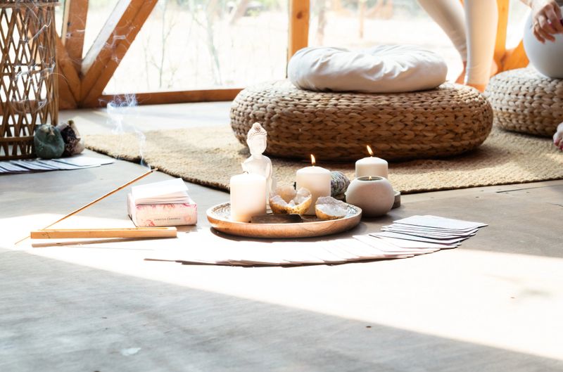 Incense sticks, candles, a buddha figurine, and cards arranged on the floor, preparing for a kundalini yoga session