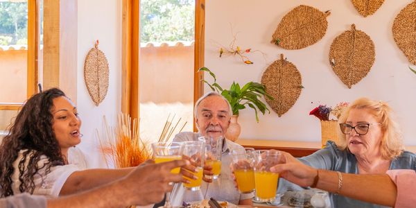 Group of people toasting with glasses of orange juice at a dining table.