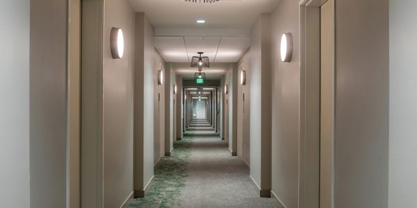 A long, modern hotel corridor with doors and wall lights.