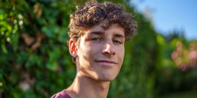 Young man smiling outdoors with greenery background.