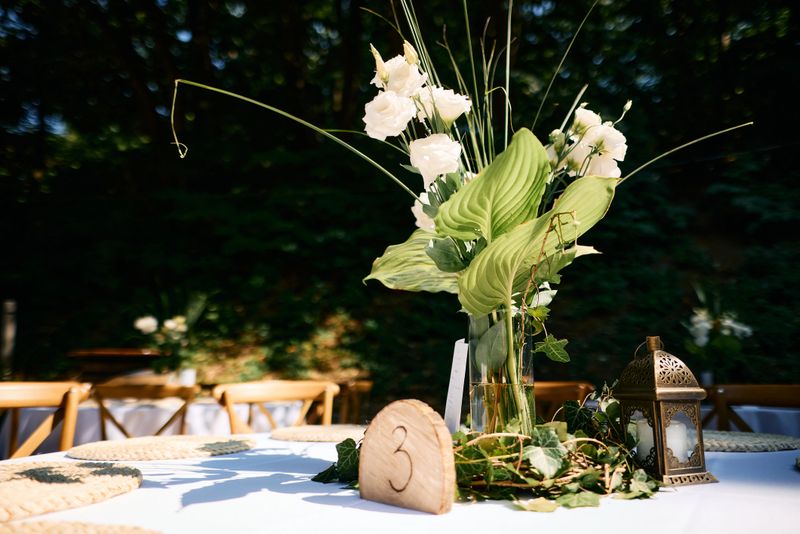 Elegant floral centerpiece, featuring white flowers and lush greenery, illuminates wedding table setting number 3, creating a romantic and enchanting atmosphere