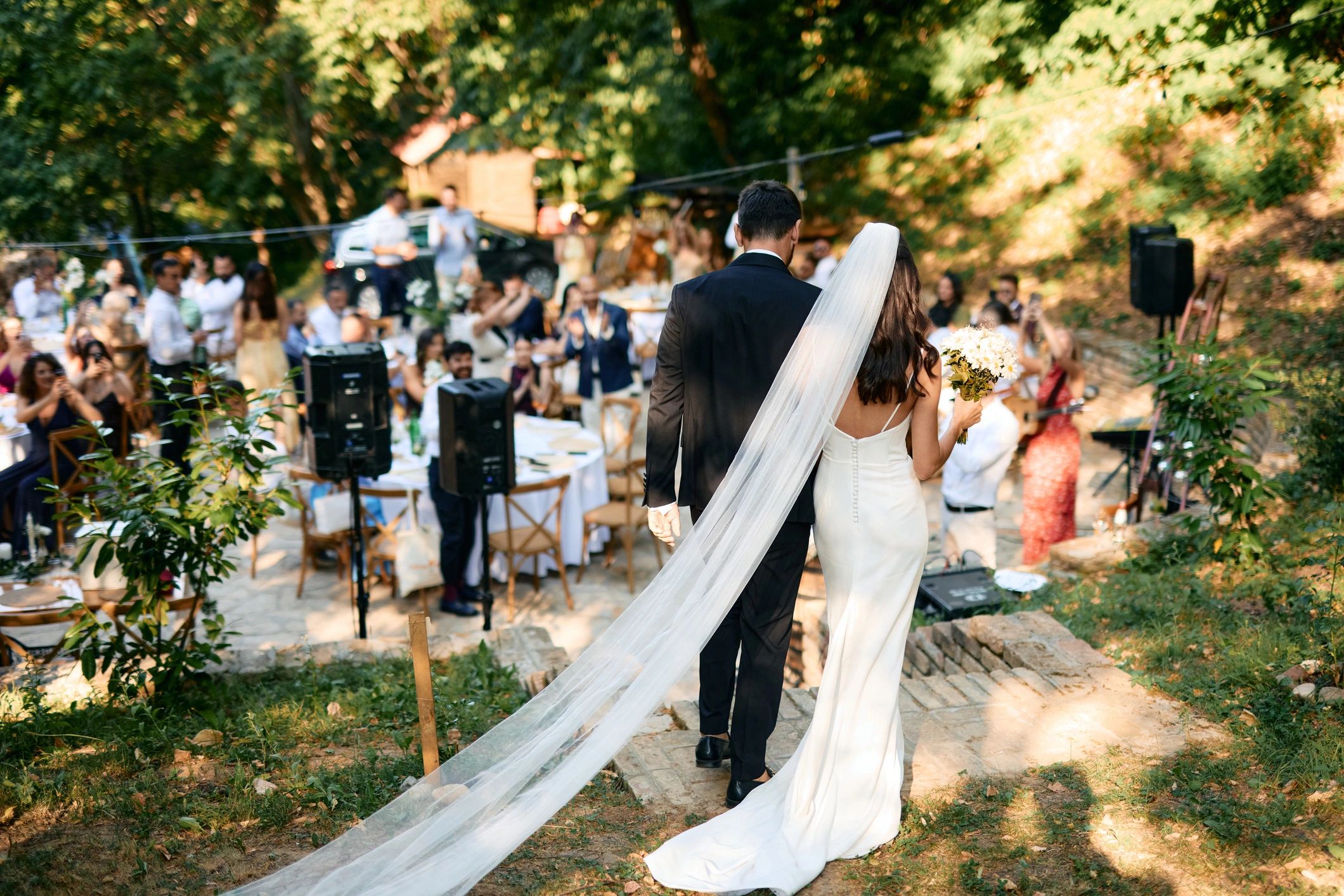 Bride and groom walking down outdoor aisle with guests applauding.
