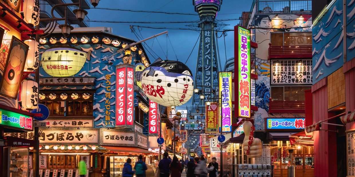 Busy street with colorful signs and lanterns in a Japanese city at dusk.
