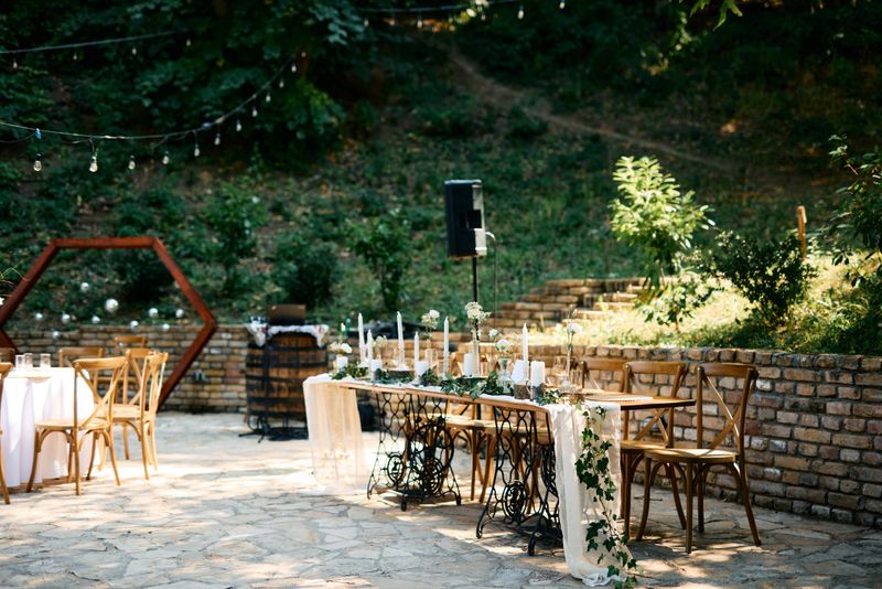 Elegant wedding reception table setting with greenery, candles, and vintage sewing machine bases in a picturesque outdoor location, creating a romantic and rustic ambiance