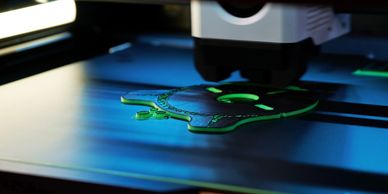 3D printer creating a green and black object with intricate details.