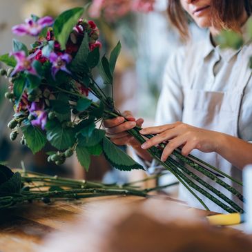 Person arranging a bouquet of colorful flowers on a wooden table.