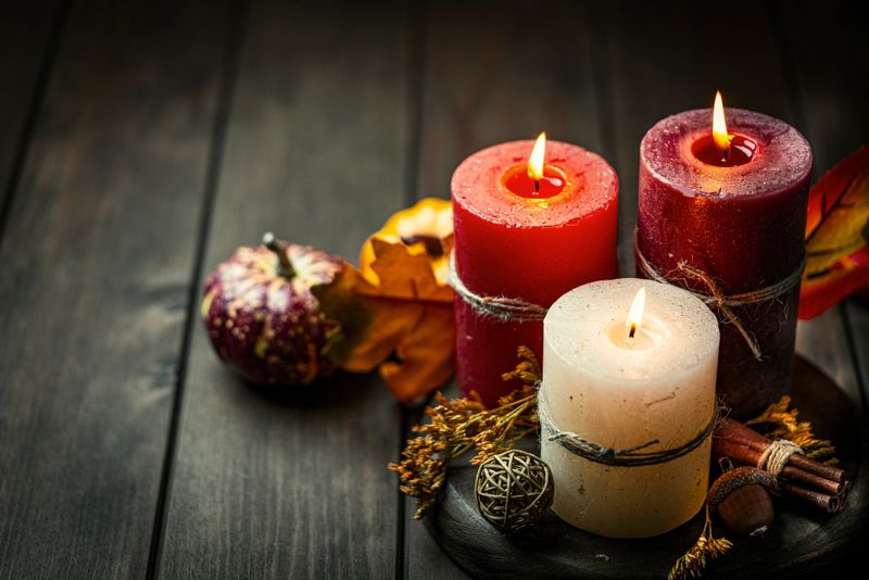 High angle view of three burning candles in a cozy atmosphere of Autumn, Thanksgiving or Christmas table. Decor with fallen leaves, nuts and pumpkin. Greeting card or copy space